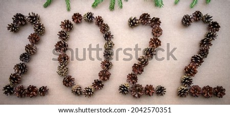 New Year's figures 2022 made of pine cones on cardboard isolate, fir branches on top. New Year's background