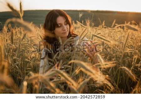 sunset, soft evening colors, a young, beautiful, emotional brunette girl with long hair on a golden wheat field. Peace, comfort in the soul, joy, nature