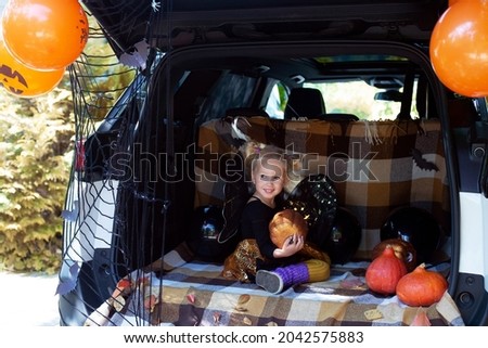 Cute little girl celebrating Halloween in car trunk. Stay home celebration. Autumn holidays. Trick or treat. Halloween in isolation
