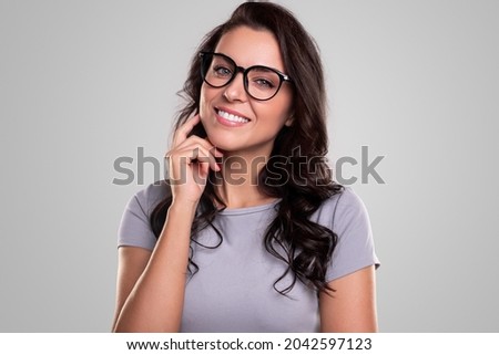 Happy young female in casual outfit and spectacles keeping hands on chest and looking at camera with amazed face expression , while standing against gray background Royalty-Free Stock Photo #2042597123