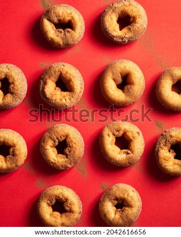 A pattern of freshly baked cinnamon donuts, display in a red background with cinnamon powder on top