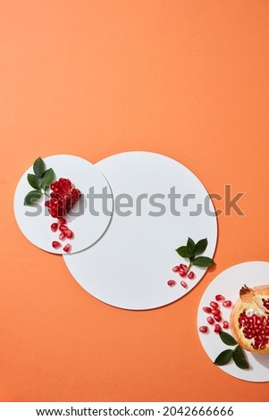 Flatlay Abstract white circle podium on orange background for cosmetics presentation with pomegranate extract. Pomegranate placed next to the product display platform. Top view image. 
