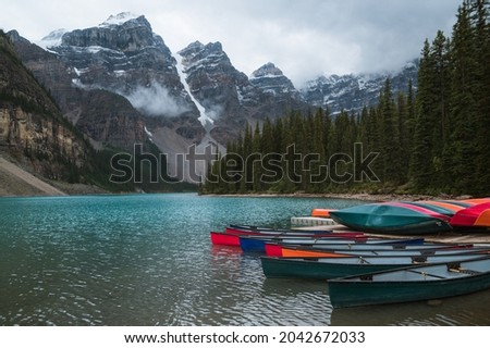 Moraine Lake with colourful canoes in foreground. Blue mountain lake in Canada with snowy rocky mountains in background.