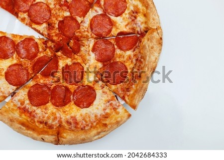 A large pepperoni pizza lies on a white surface, cut into pieces, an Italian dish, a top view, a place for text. Pizza with sausage and cheese. Improper nutrition, weight gain