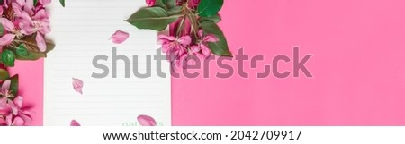 Top view of blank sheet of notebook and branches of apple blossoms on pink background. Copy space. Banner