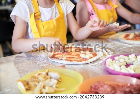 Child wearing yellow apron, putting ingredients dough on the table. Close-up picture of hands, making topping for pizza. Bakery master class for small children. Pizza workshop at juniors' party.