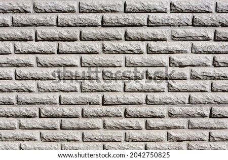 A gray wall, lined with tiles in a texture similar to torn bricks