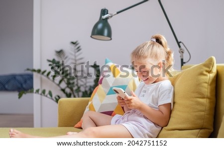 Little girl watching cartoons on her phone.Child is using mobile phone. Kid having fun and looking at screen of devices. Technology concept. 