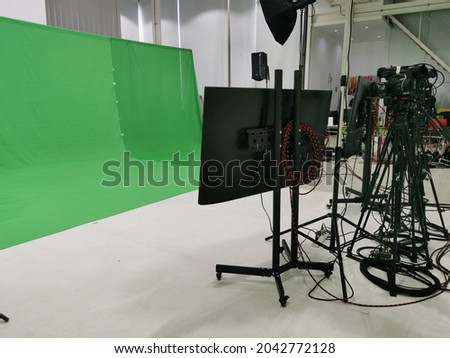 Oblique back view of a display monitors, video camera sets on tripods, and softbox lights equipment, set up in front of a green screen cloth backdrop, get ready making a video shoot in the studio.