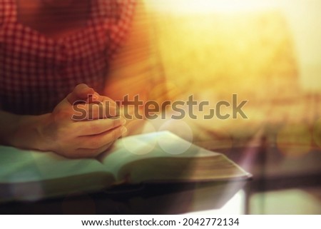 Close up of a woman hands praying on the open holy  bible on a table indoor with the windows light lay warm tone . Christian faith and trust concept  with copy space. Christian devotional background. Royalty-Free Stock Photo #2042772134