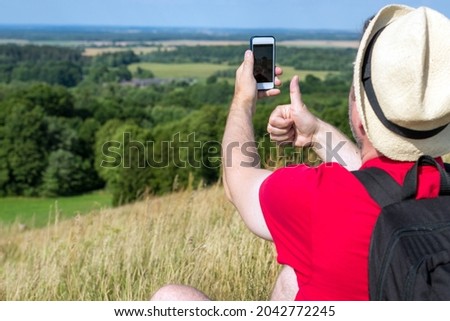 Young backpacker man taking selfie picture using smartphone and showing thumb up cloudy sky weather mountain summer range.Active sport backpacking healthy lifestyle concept.