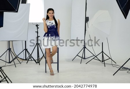 Young asian model posing in white photography scene. The atmosphere in the photo studio with a complete set of photographic equipment such as  Soft-box, Flash Reflector and tripod stand.