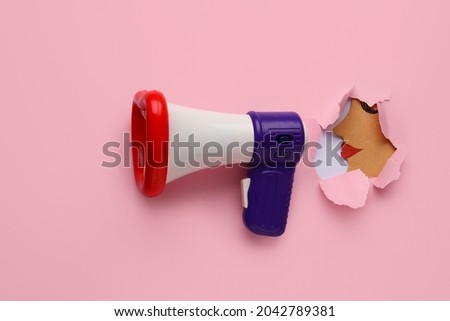 Toy megaphone and paper head visible through torn color paper