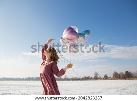 Profile portrait of tender happy teenage girl in pink dress holding many colorful balloons in her hands on a sunny winter day. feels great, festive, enjoys the moment. Beautiful birthday girl
