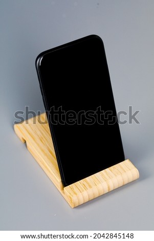 A black smartphone on a wooden stand is lying on the table. A place to copy.