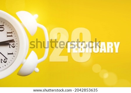 February 20th. Day 20 of month, Calendar date. White alarm clock on yellow background with calendar day. Winter month, day of the year concept