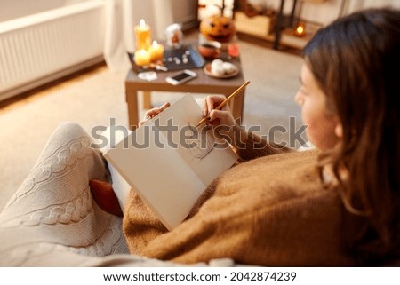 halloween, holidays and leisure concept - young woman with pencil drawing pumpkin in sketchbook or diary at cozy home