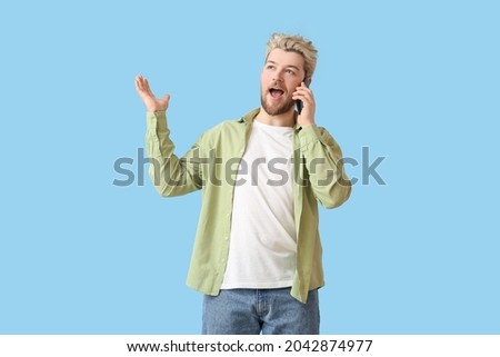 Young man talking by mobile phone on color background