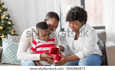 family, winter holidays and people concept - happy african american mother, father and baby son opening gift box at home on christmas