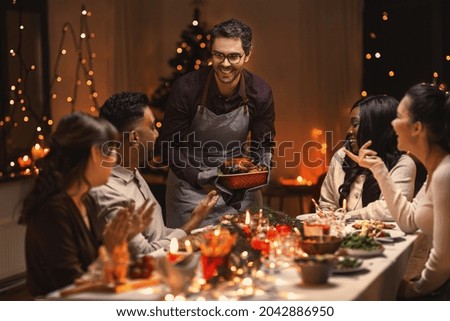 holidays and celebration concept - multiethnic group of happy friends having christmas dinner at home Royalty-Free Stock Photo #2042886950
