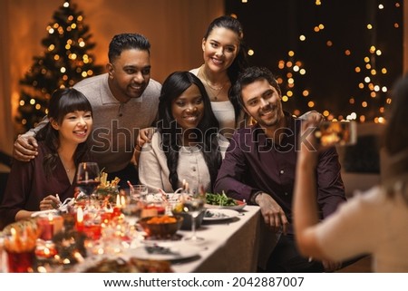 holidays, party and celebration concept - multiethnic group of happy friends having christmas dinner and photographing at home