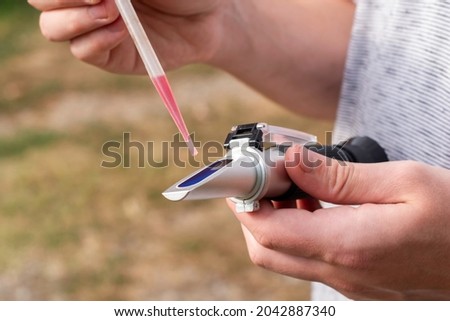 the winemaker applies a drop of grape juice with a pipette to the prism of a refractometer to determine the amount of sugar in the grape juice. High quality photo