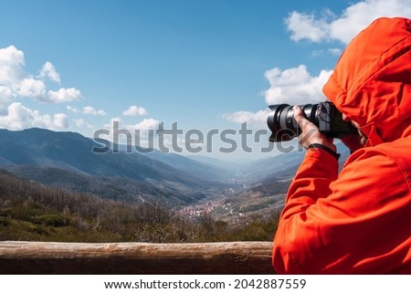 Close-up of an unrecognizable photographer in a red coat taking a photo of the mountains landscape with a blue sky with some clouds. copy space