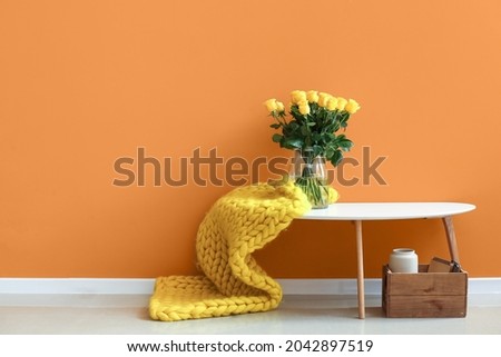 Vase with beautiful yellow roses on table near color wall in room