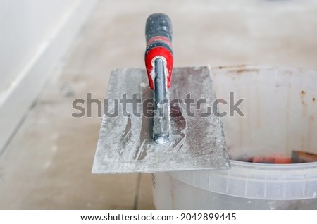 Craft, refurbishment and renovation concept: Close-up of a trowel or spatula on the edge of a bucket on a construction site in the interior, selective focus, lots of copy space