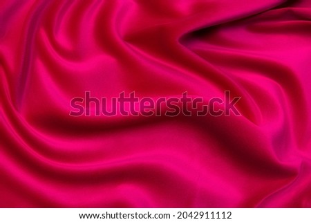 Close-up texture of natural red or pink fabric or cloth in same color. Fabric texture of natural cotton, silk or wool, or linen textile material. Red and orange canvas background. Royalty-Free Stock Photo #2042911112