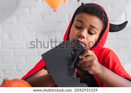 african american boy in halloween costume cutting carton with scissors