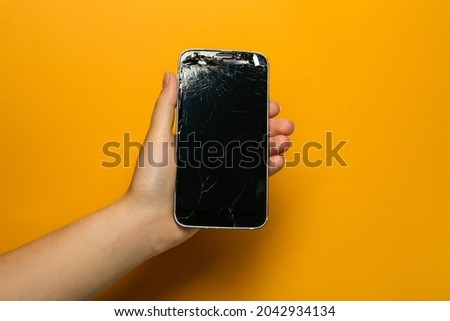 Woman holding damaged smartphone on orange background, closeup. Device repairing