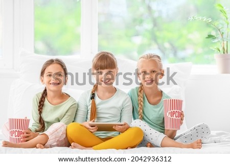 Cute little girls with tablet computer and popcorn at home
