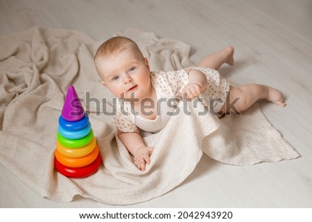 cute baby is lying in bodysuit on the floor of the house playing with an educational toy. High quality photo