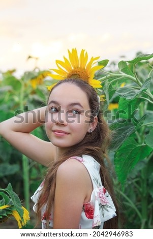 Beautiful teen girl is smiling with sunflower in summer field
