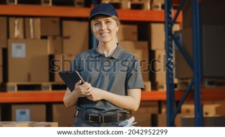Female Manager Using Tablet Computer To Check Inventory, Smiles and Looks at Camera. Warehouse Retail Center with Cardboard boxes,  e-Commerce Online Orders, Food. Frontline Hero. Royalty-Free Stock Photo #2042952299