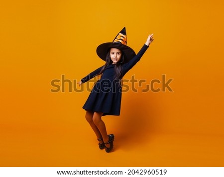 Little cheerful Caucasian girl in Halloween witch costume isolated on yellow background.