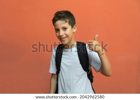 Elementary schoolboy with thumb up isolated against an orange wall. back to school concept.