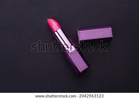 Make-up mock up with opened lipstick tube and purple cap on black background.