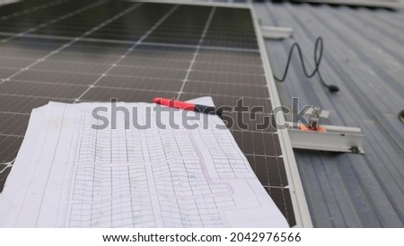 Close up of worker installing and working on maintenance of photovoltaic panel system installed. In the foreground is a diagram of the installation of solar panels. Solar panels on roof top.