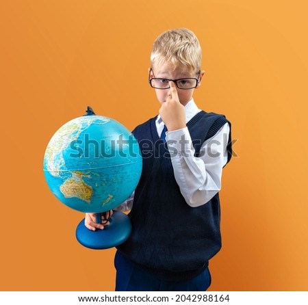 School boy in glasses, in a dark blue vest and a white shirt with a globe in his hands on an orange background. A political map of the World.