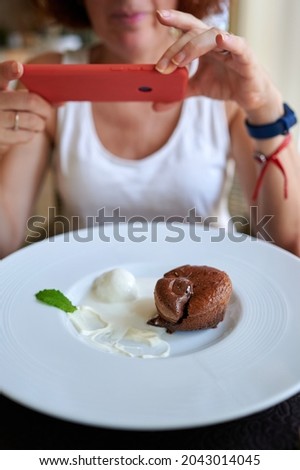Woman taking picture with the smart phone a chocolate dessert with ice cream, Vertical shot