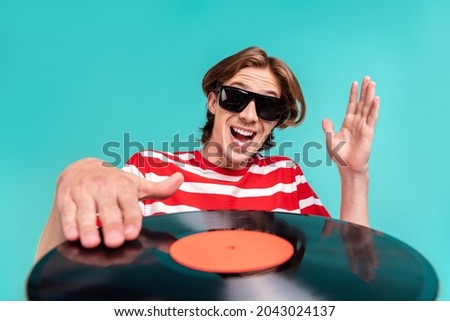 Portrait of attractive funky cheerful deejay guy playing vinyl disk isolated over bright teal turquoise color background