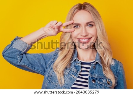 Portrait of gorgeous positive charming lady show v-sign cover eye white smile on yellow background