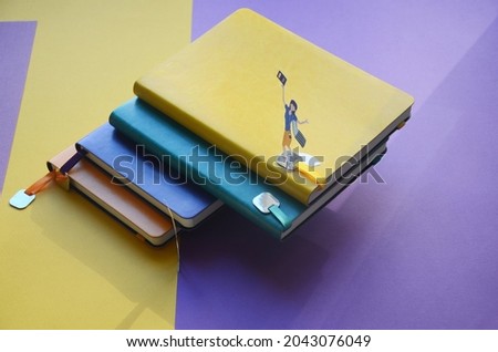 Composition from notebooks and pens on a colored background. Small figures of people cut out of paper. Bright colored notebooks. Handles of all colors.