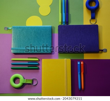 Bright notepads and colored pens on a background of colored paper. Writing accessories. Corporate gifts for office employees. Sunny mood for work.