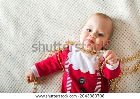 Baby 9 months old dressed as Santa Claus and New Year's beads on white plaid close-up and copy space.