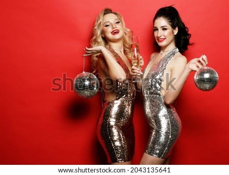 Party and celebration concept: Two glamour women, girlfriends in luxury glitter sequins dress and bright visage holding disco balls and glass of wine,
