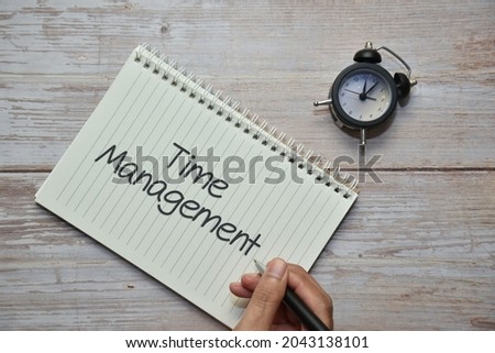 Holding a pen with TIME MANAGEMENT on notebook and analog alarm clock. Business concept.