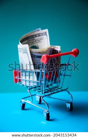 concept - curled dollar banknotes fall out of Shopping Cart Trolley against the green background